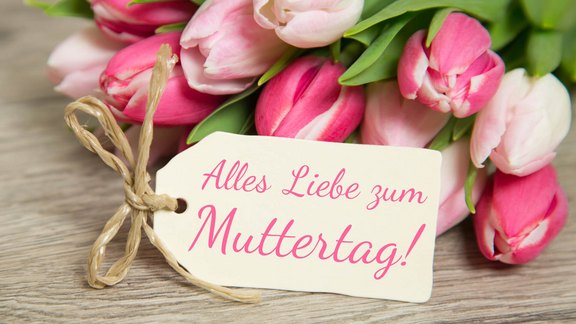 Ein Strauß rosa Tulpen mit einem Geschenkanhänger, auf dem 'Alles Liebe zum Muttertag!' steht.